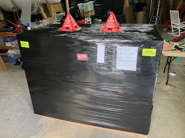 Large rectangular item wrapped in black film with handling labels